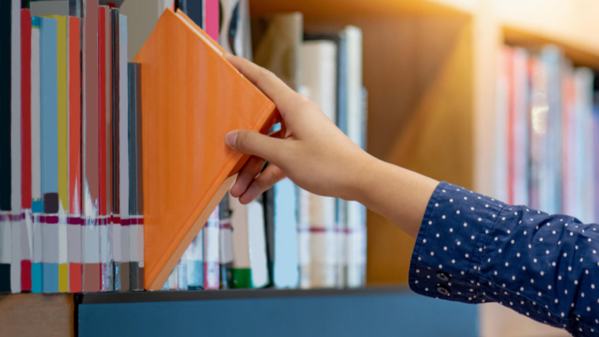 A person selecting a book from a shelf lined with various literature